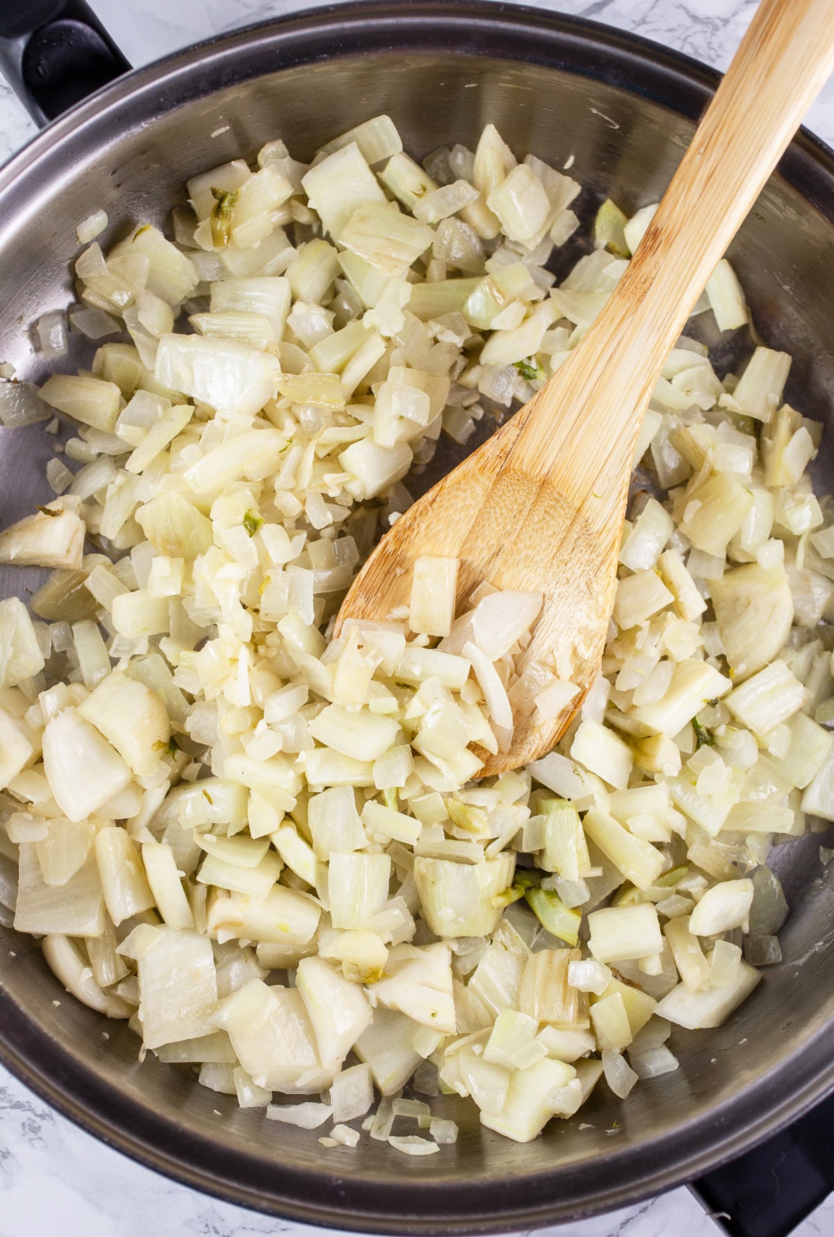 Garlic, onions, and fennel sautéed in skillet with wooden spoon.