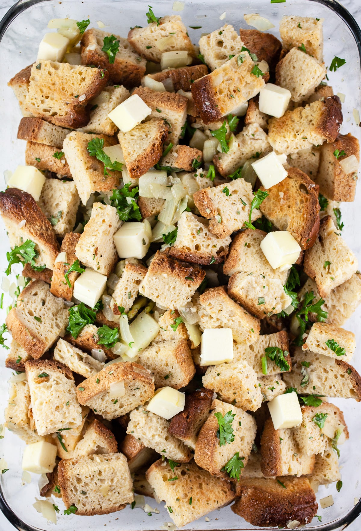 Uncooked stuffing dotted with butter in glass casserole dish.