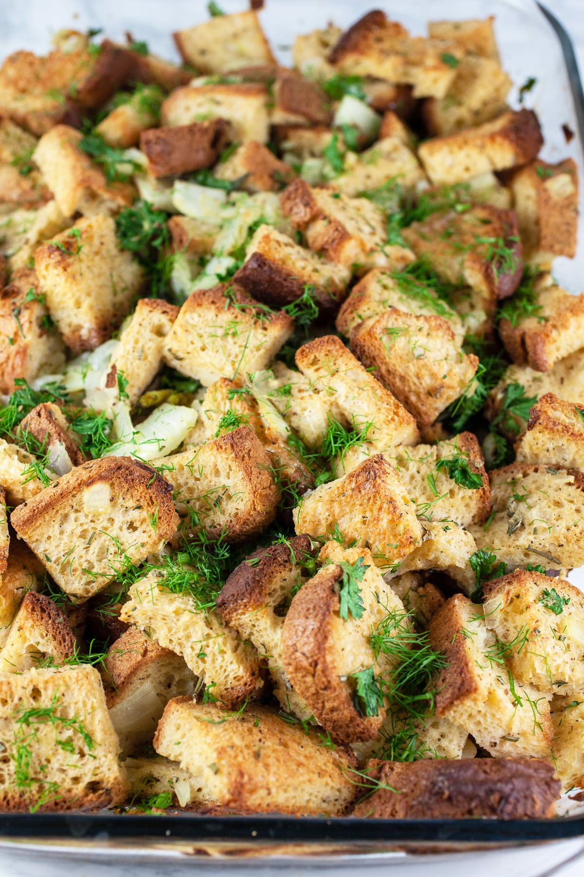 This Savory Fennel and Spinach Stuffing recipe is the perfect side dish for Thanksgiving dinner! It's healthy vegetarian comfort food at its best. This stuffing is made with toasted bread cubes and sauteed fennel. It's baked in the oven and super moist. This homemade stuffing is a unique take on a classic traditional dish. Stuffing from scratch is the best! #stuffing #fennel #spinach #thanksgiving #sides #recipes Baked fennel herb stuffing in glass casserole dish.