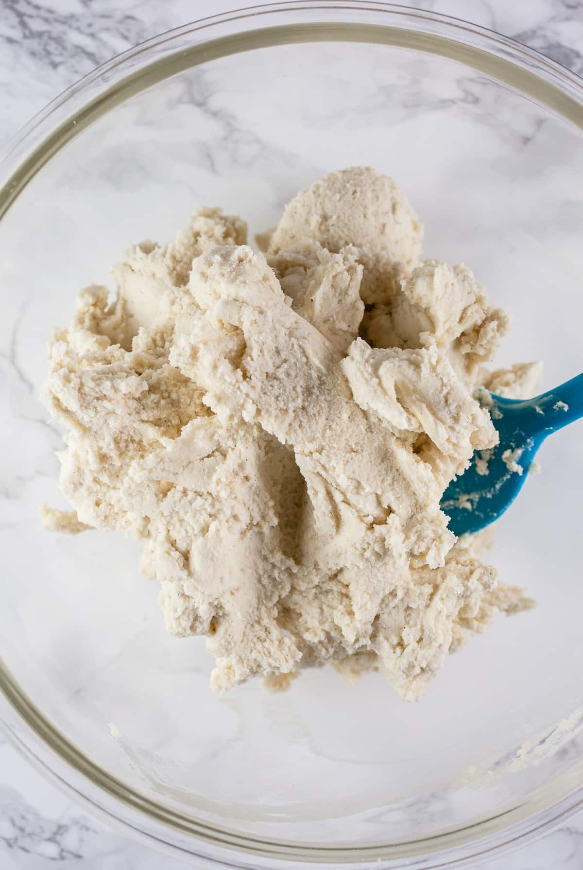 Shortbread cookie dough in glass bowl with blue spatula.