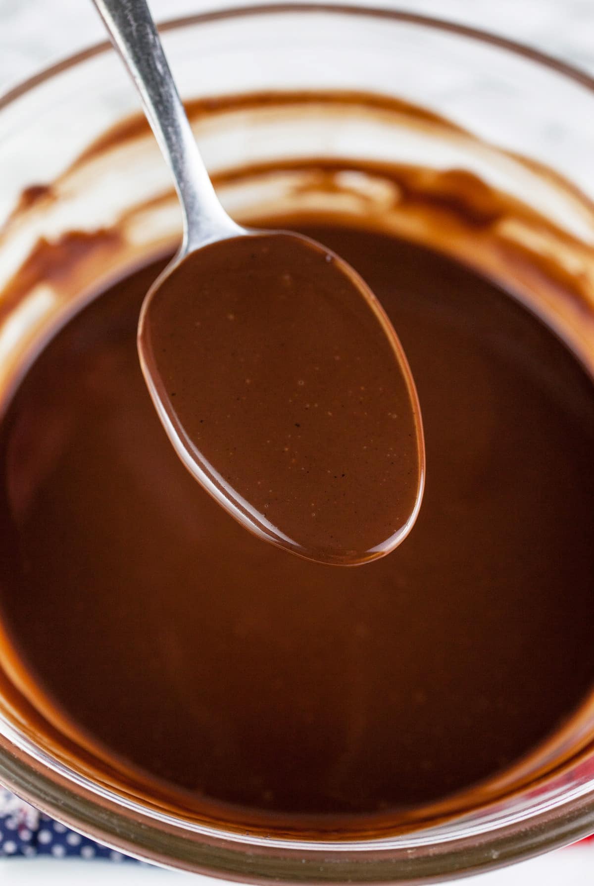 Spoonful of chocolate ganache lifted from small glass bowl.