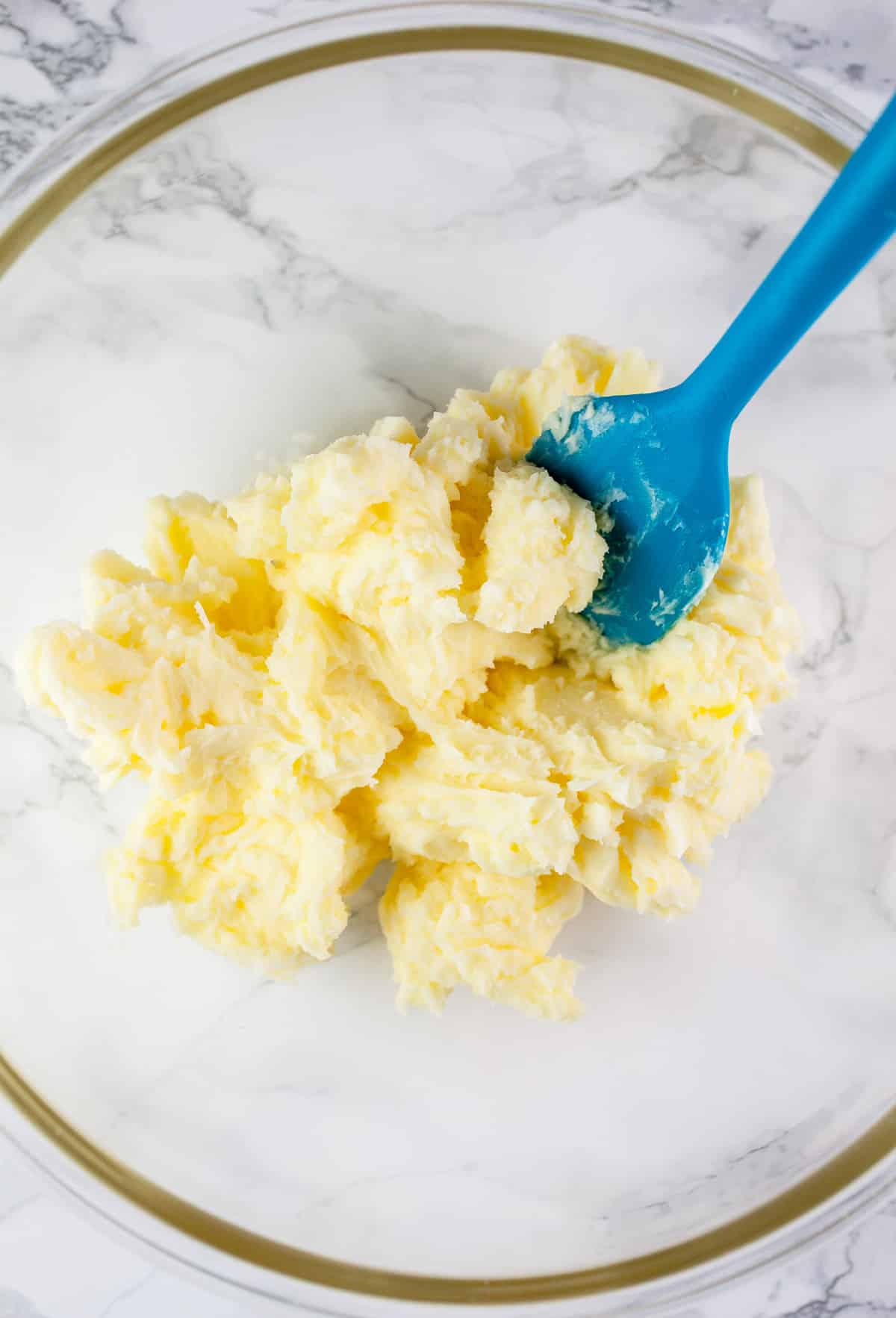 Butter and powdered sugar mixture in glass bowl with blue spatula.