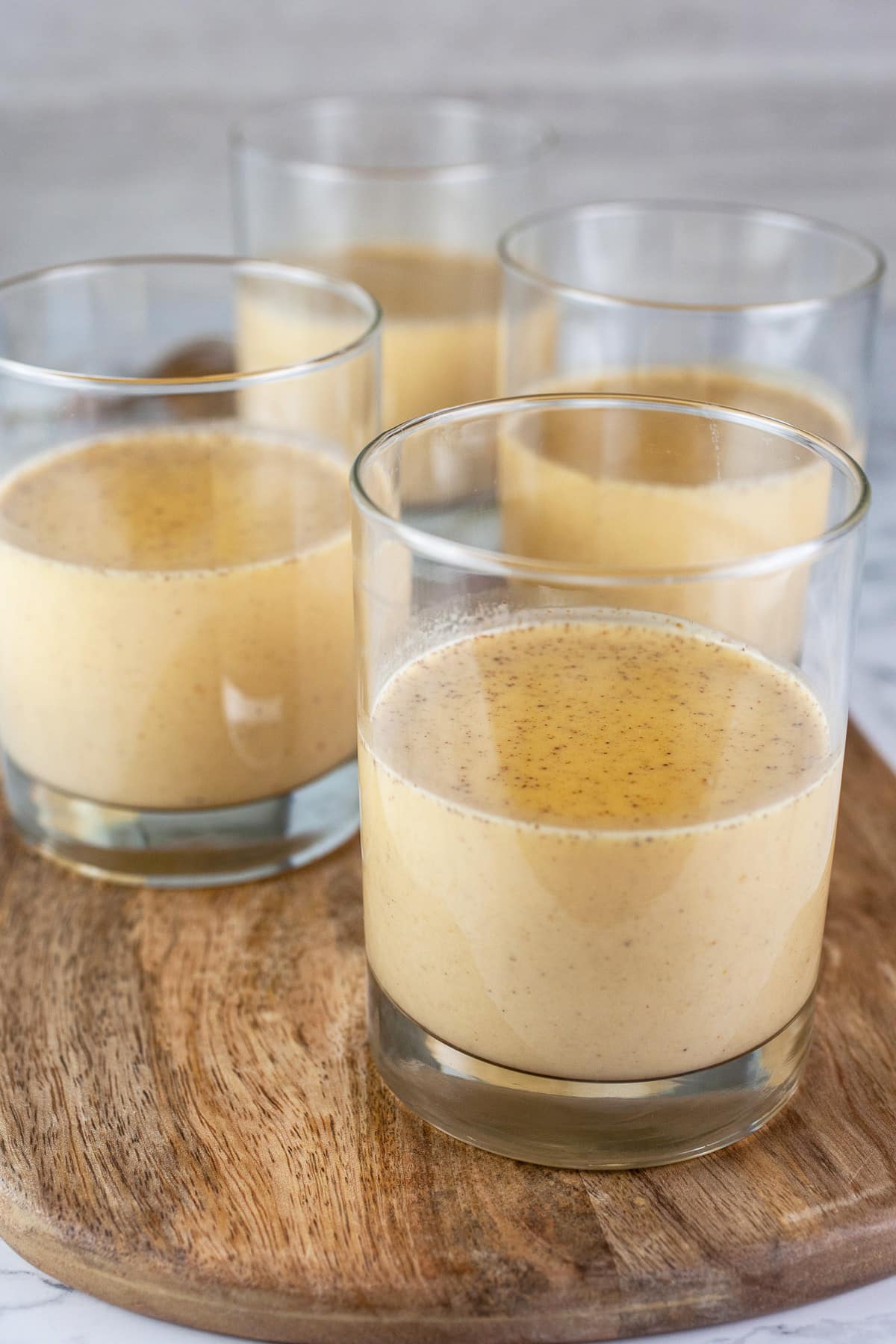 Unrefrigerated panna cotta mixture in small glasses on wooden board.