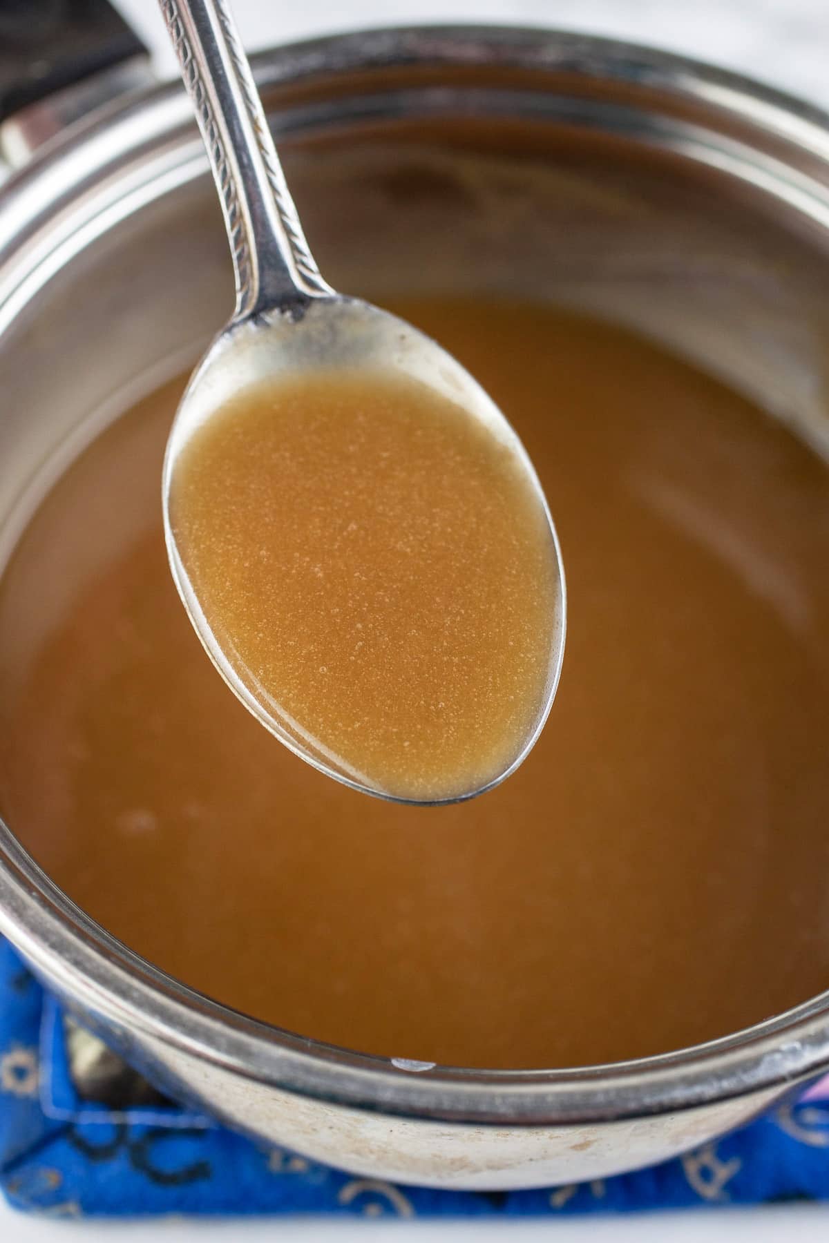 Spoonful of caramel sauce lifted from small sauce pan.