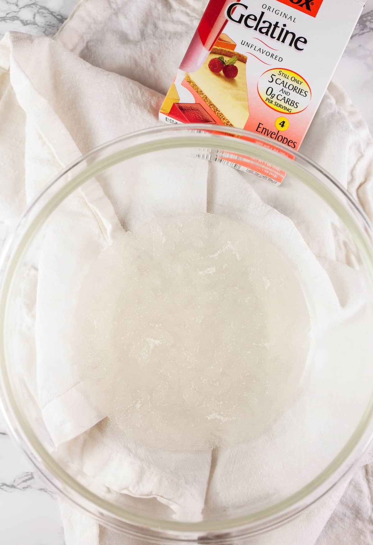 Water and gelatin in small glass bowl with white towel.