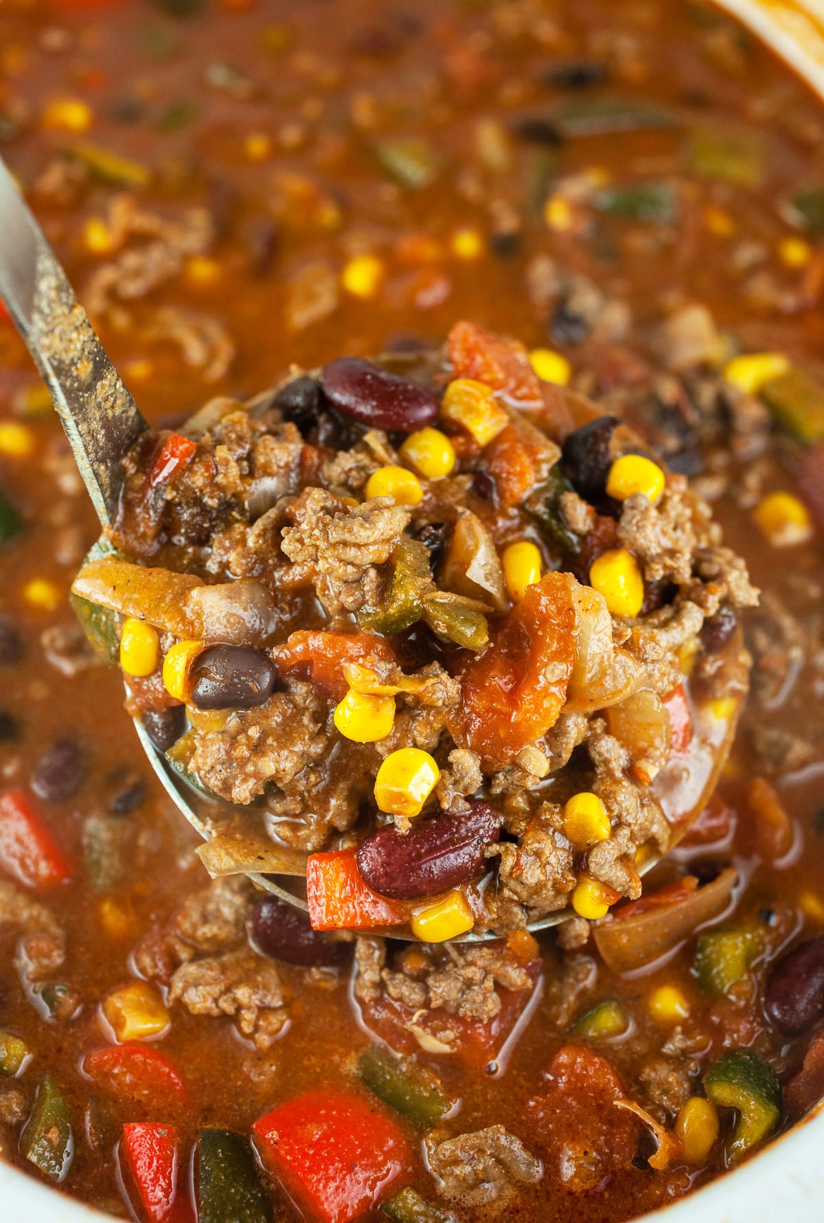 Scoop of ground beef chili lifted from slow cooker on metal ladle.