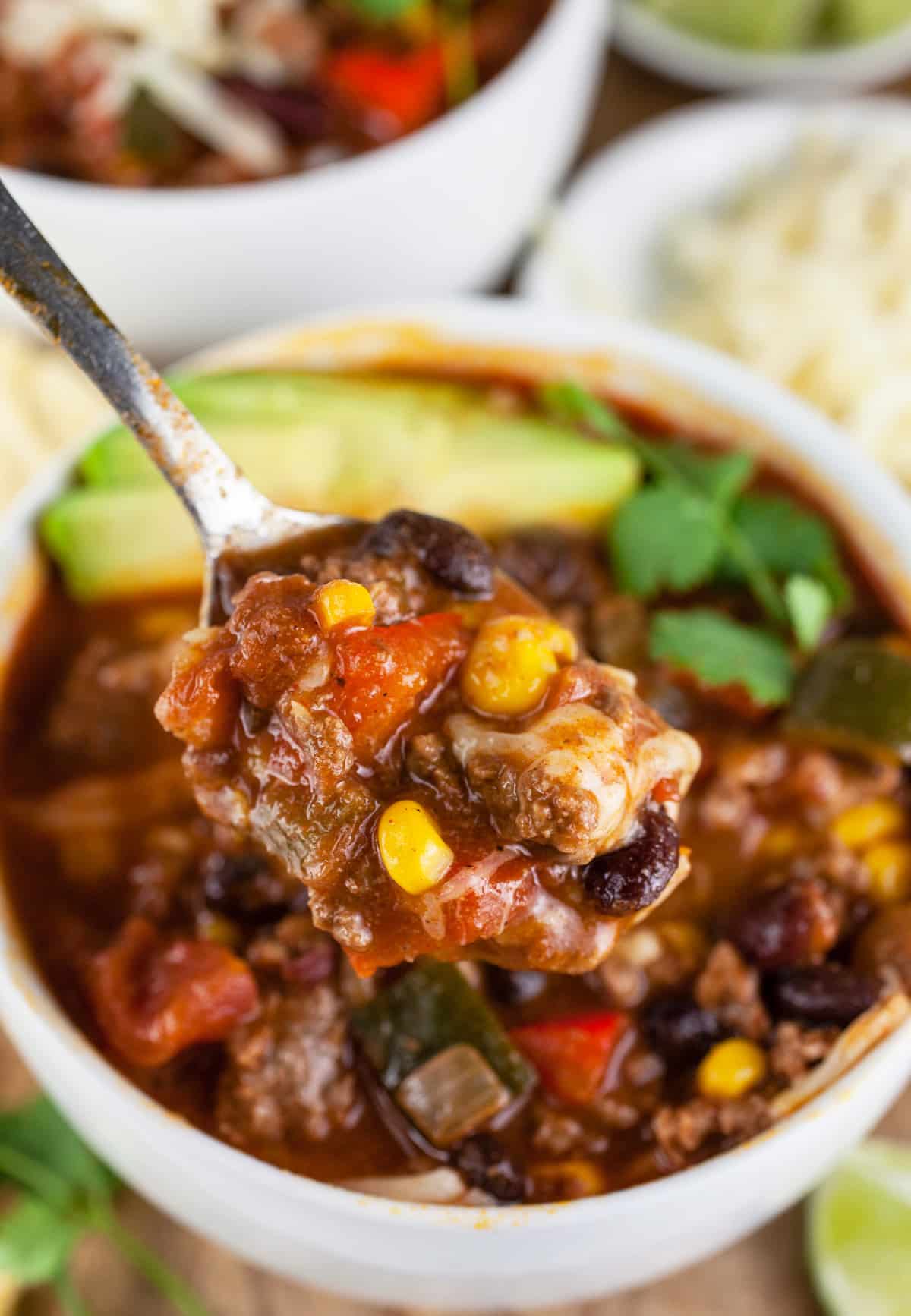 Spoonful of ground beef chili lifted from white bowl.