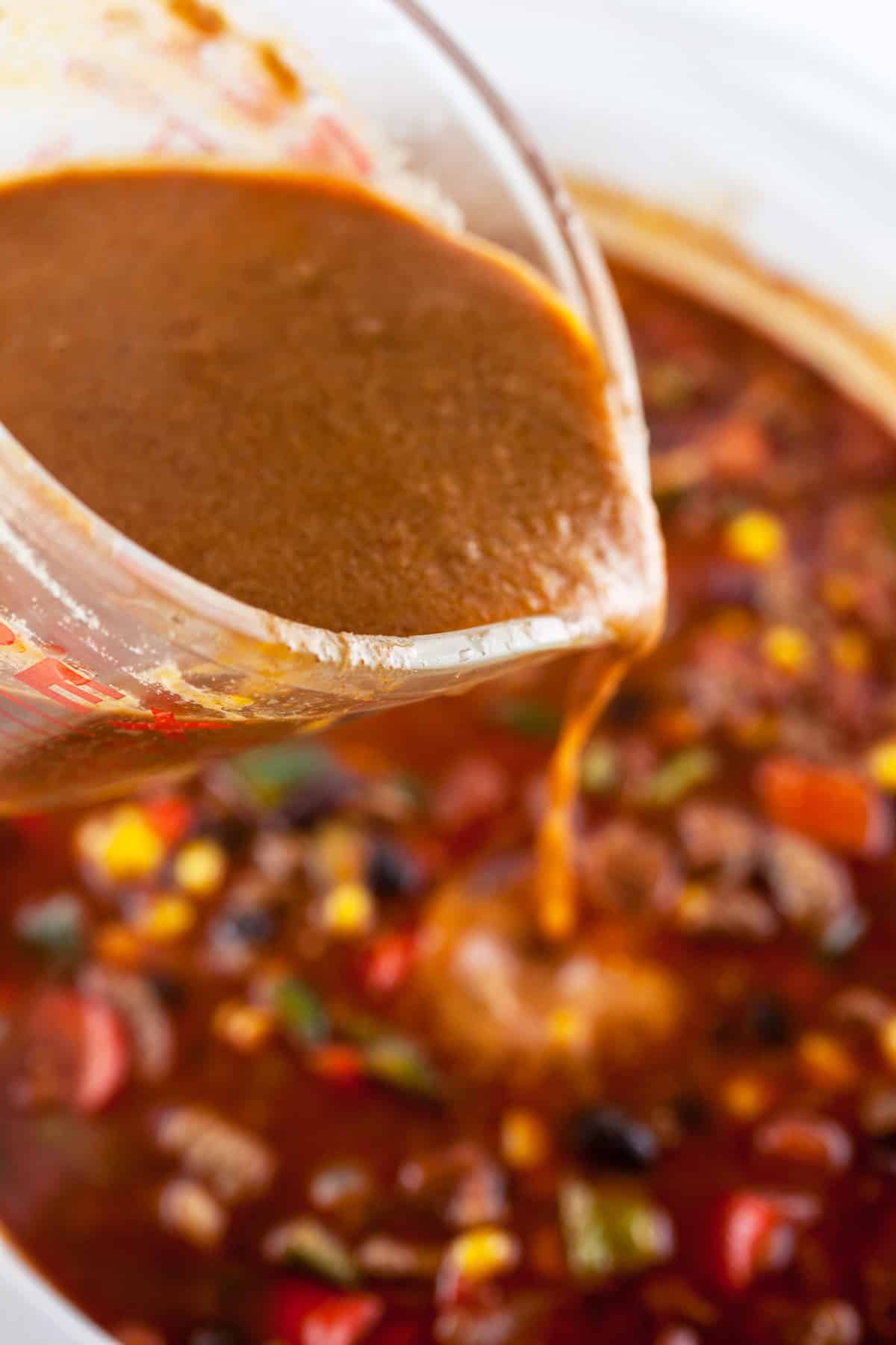 Masa harina mixture poured into slow cooker from glass measuring cup.