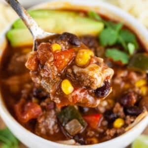 Spoonful of ground beef chili lifted from white bowl.