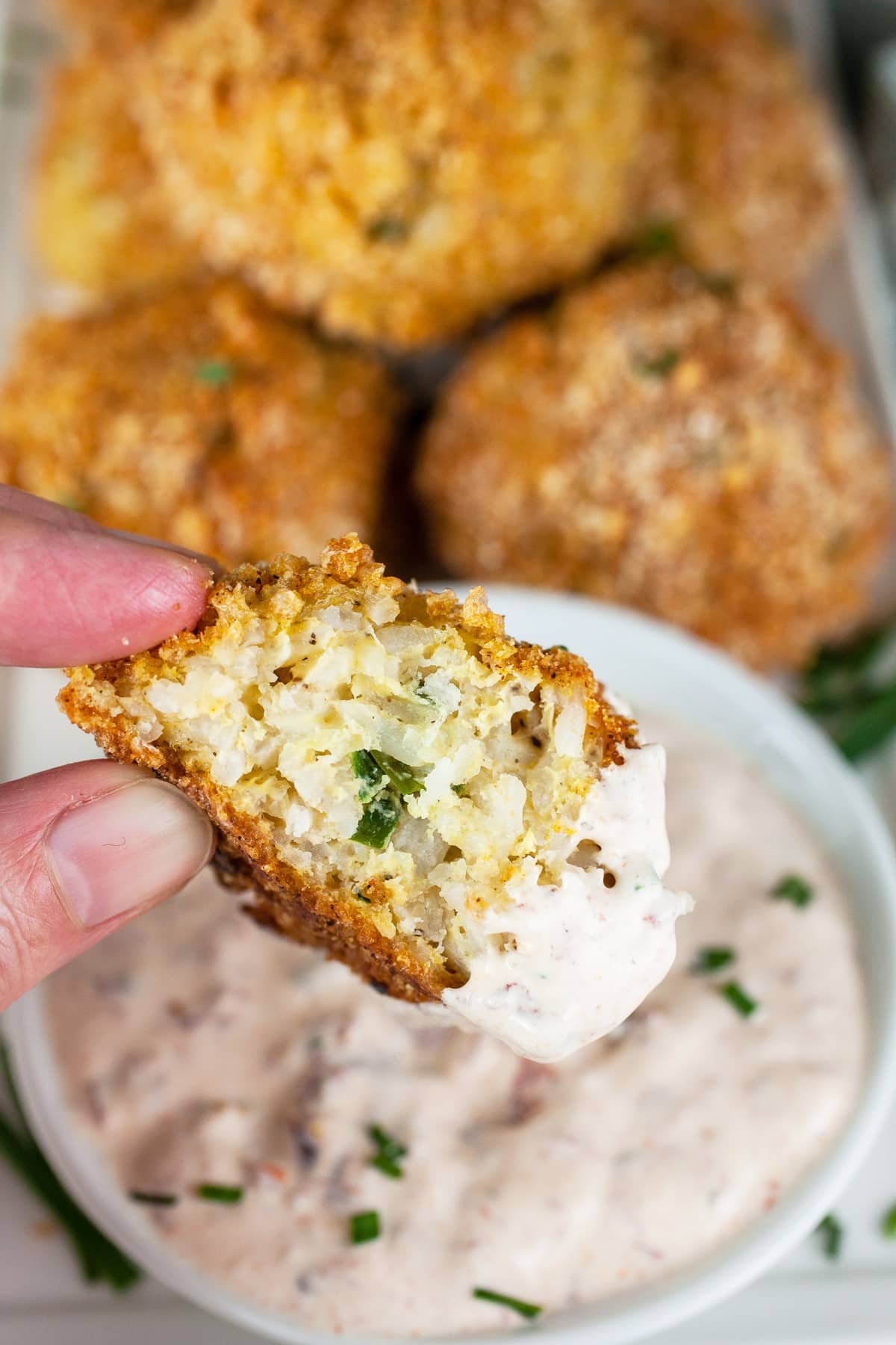 Half of a rice ball dipped into small white bowl of chipotle sour cream.