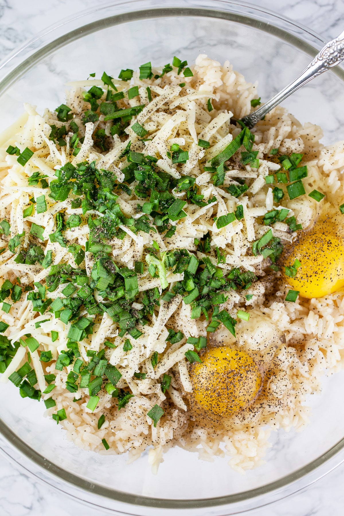 Rice, eggs, shredded cheese, and herbs in glass mixing bowl.