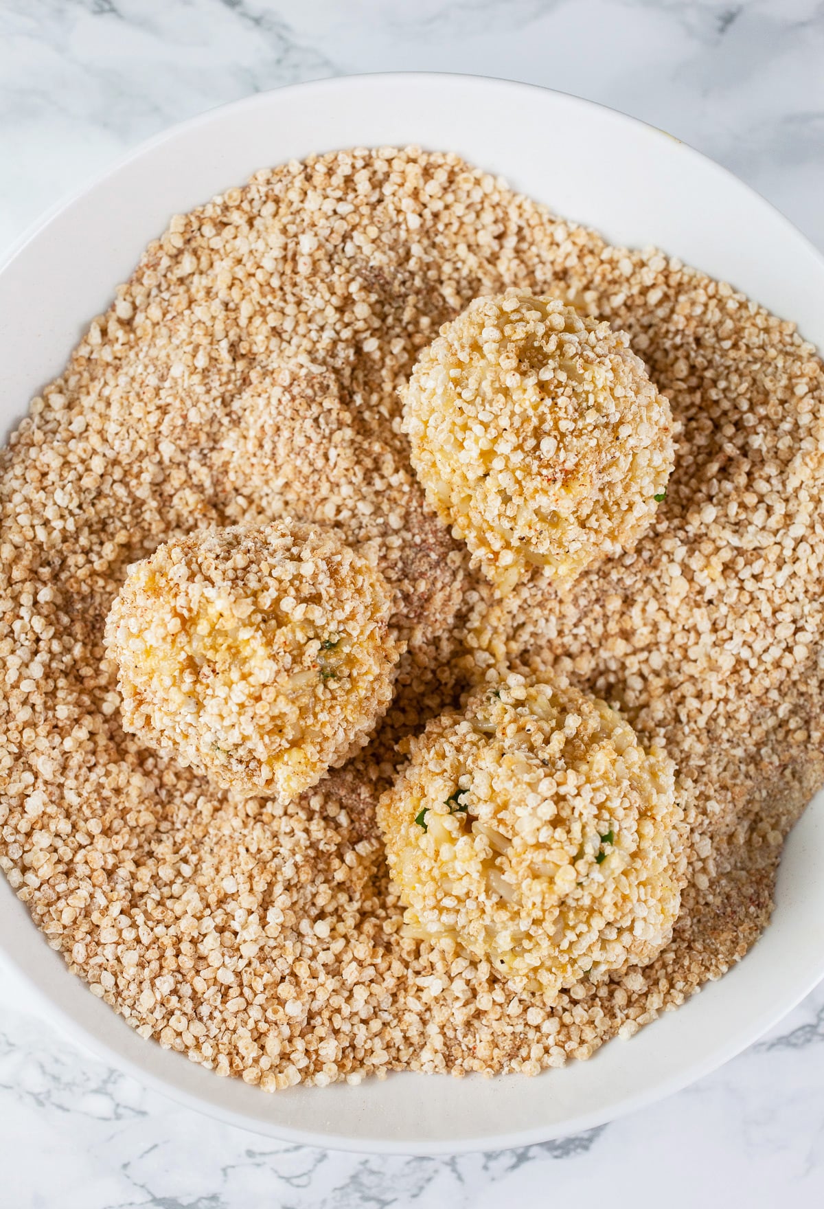 Rice balls coated in breadcrumb mixture in white bowl.