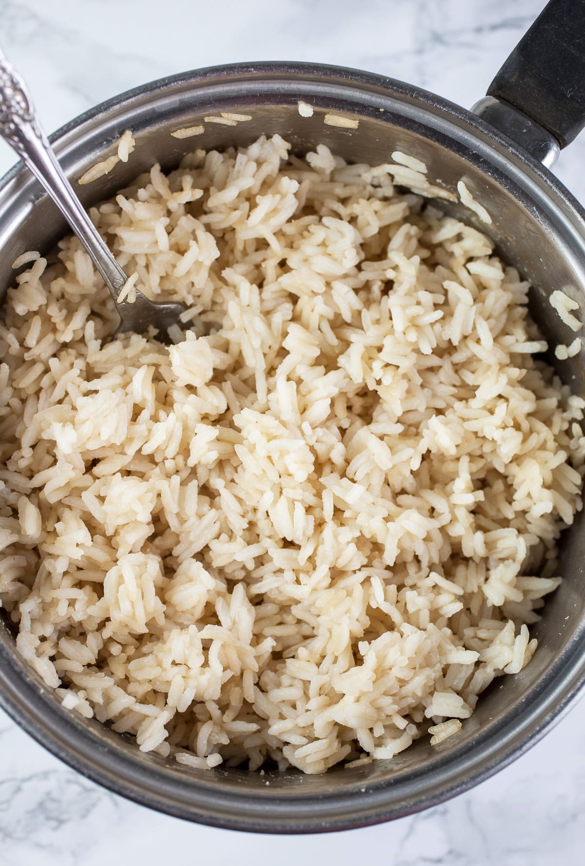 Cooked rice in sauce pan with spoon.