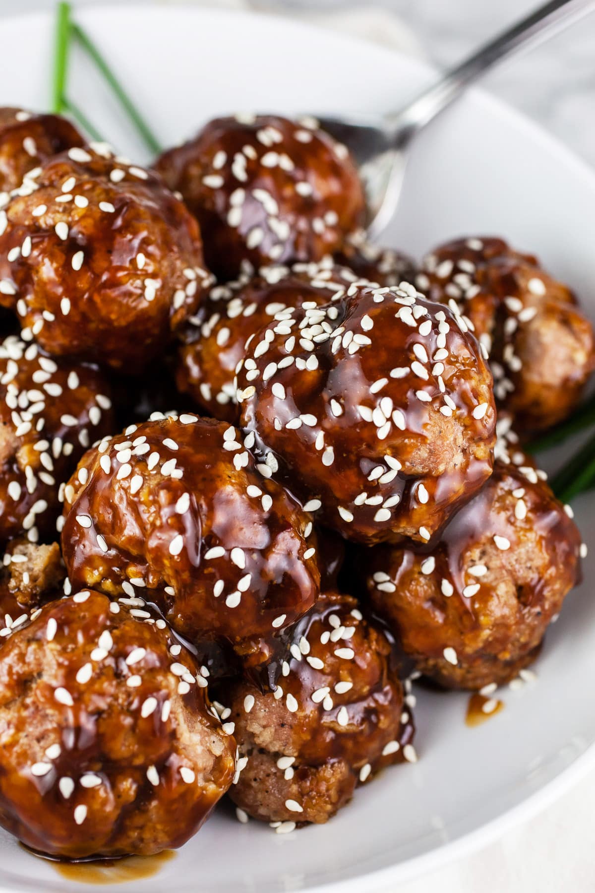 These Crockpot Teriyaki Meatballs are easy to make and full of flavor! These Asian meatballs are made with turkey, baked in the oven, and covered with a sticky sweet and savory sauce. They're warmed in the slow cooker so they're great for holiday parties like Christmas and New Year's Eve. Also great for Game Day. They're gluten free as well! #crockpot #meatballs #turkey #teriyaki #glutenfree Teriyaki turkey meatballs with sesame seeds in white bowl.