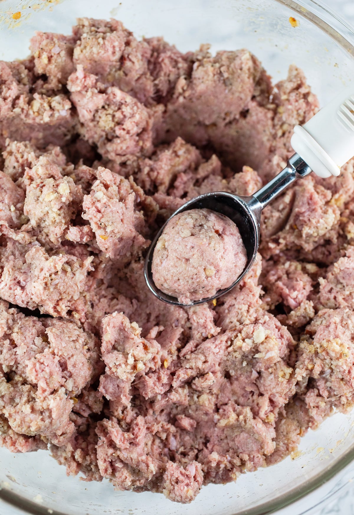 Ground turkey mixture in large glass bowl with ice cream scoop.