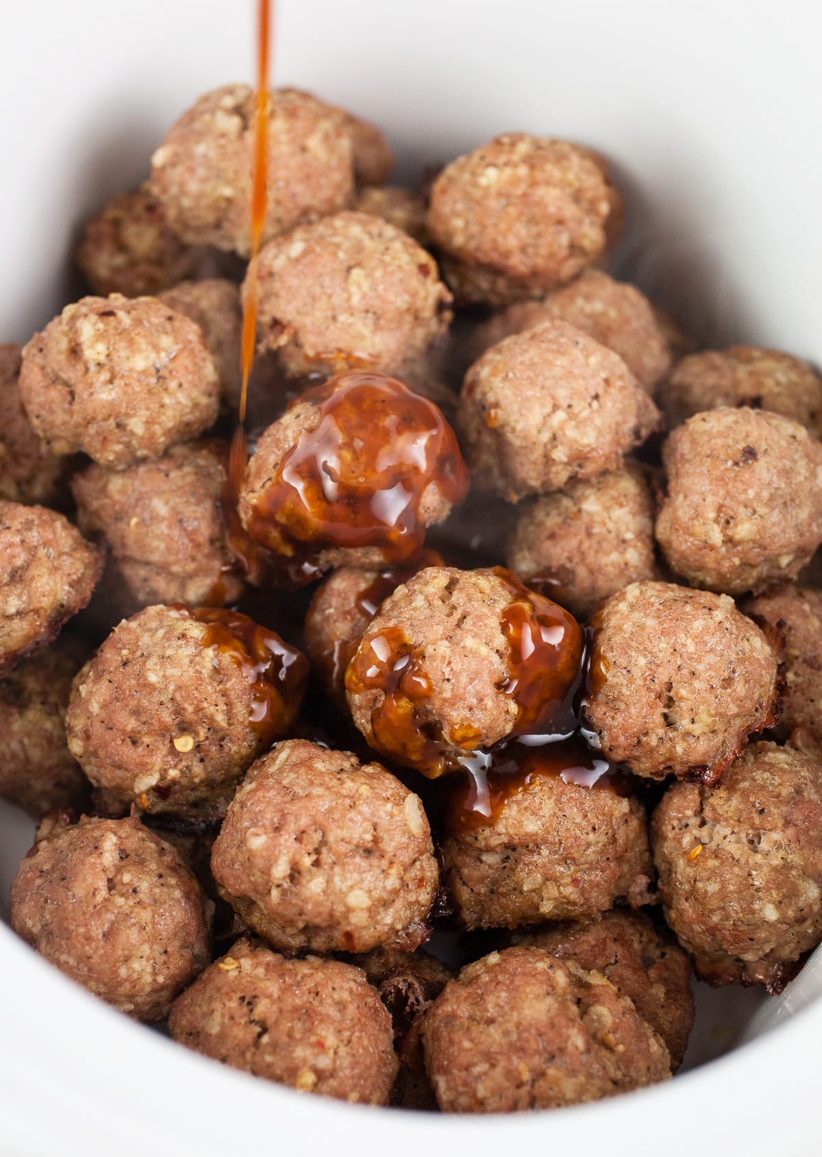 Teriyaki sauce poured over meatballs in slow cooker.