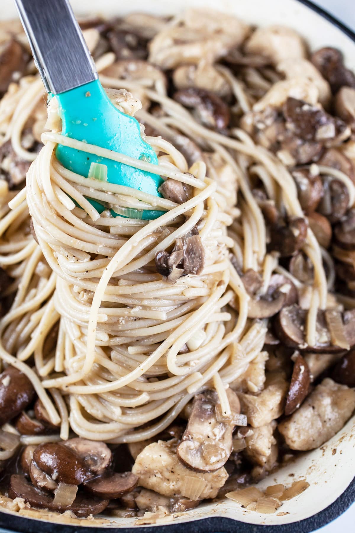 Chicken marsala pasta lifted from skillet using tongs.