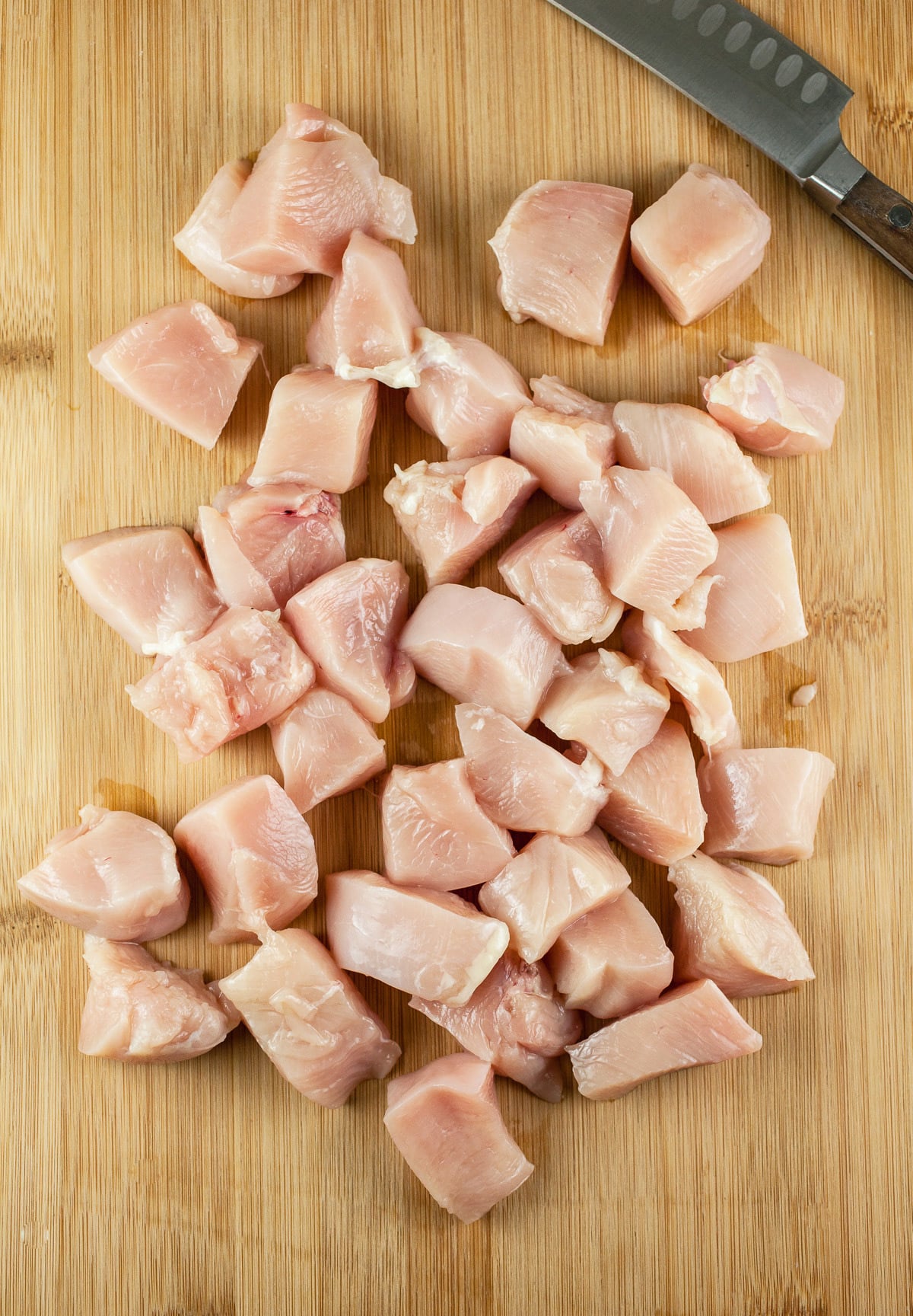 Raw chicken breasts cut into chunks on wooden cutting board.