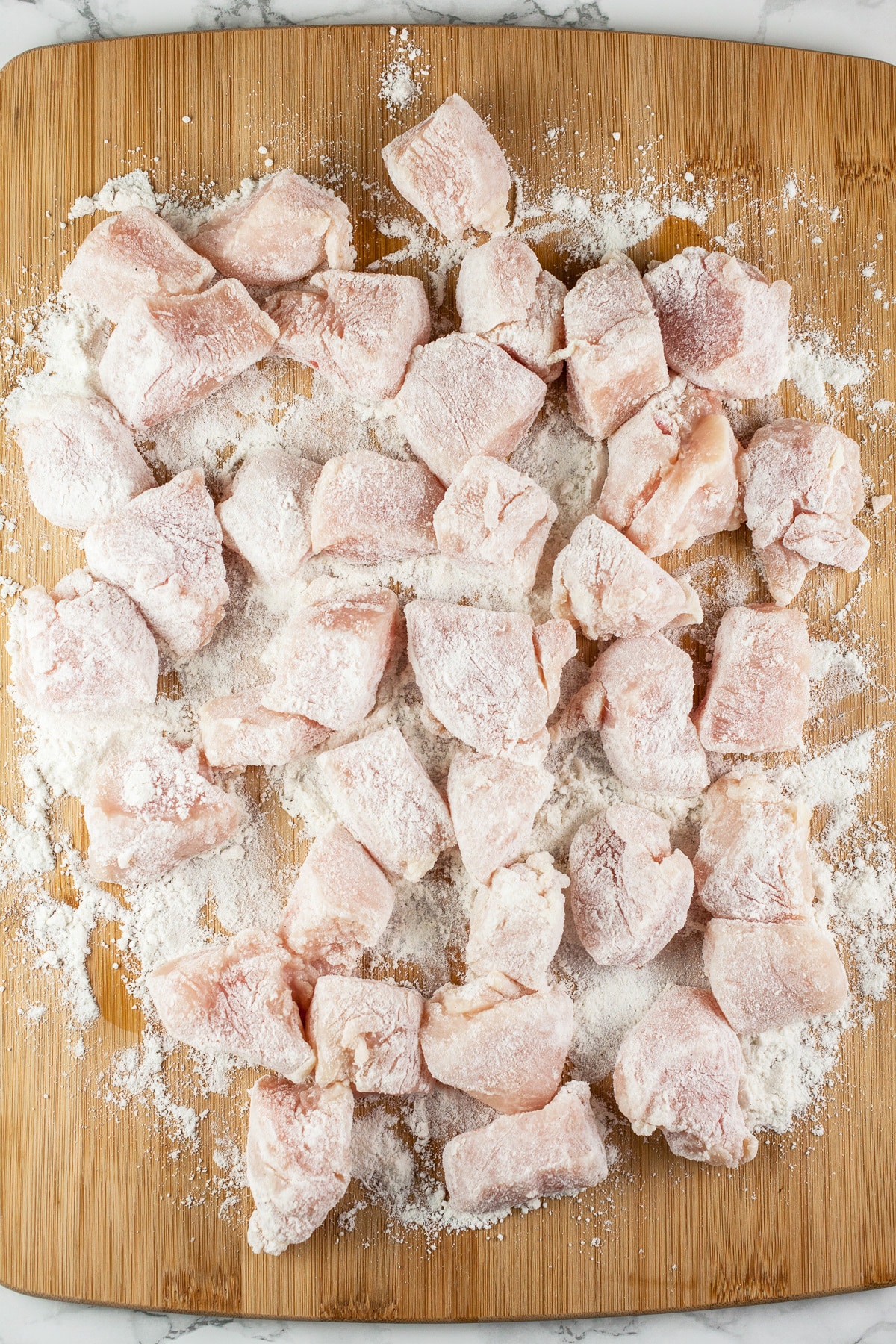 Raw chicken breasts coated in flour on wooden cutting board.