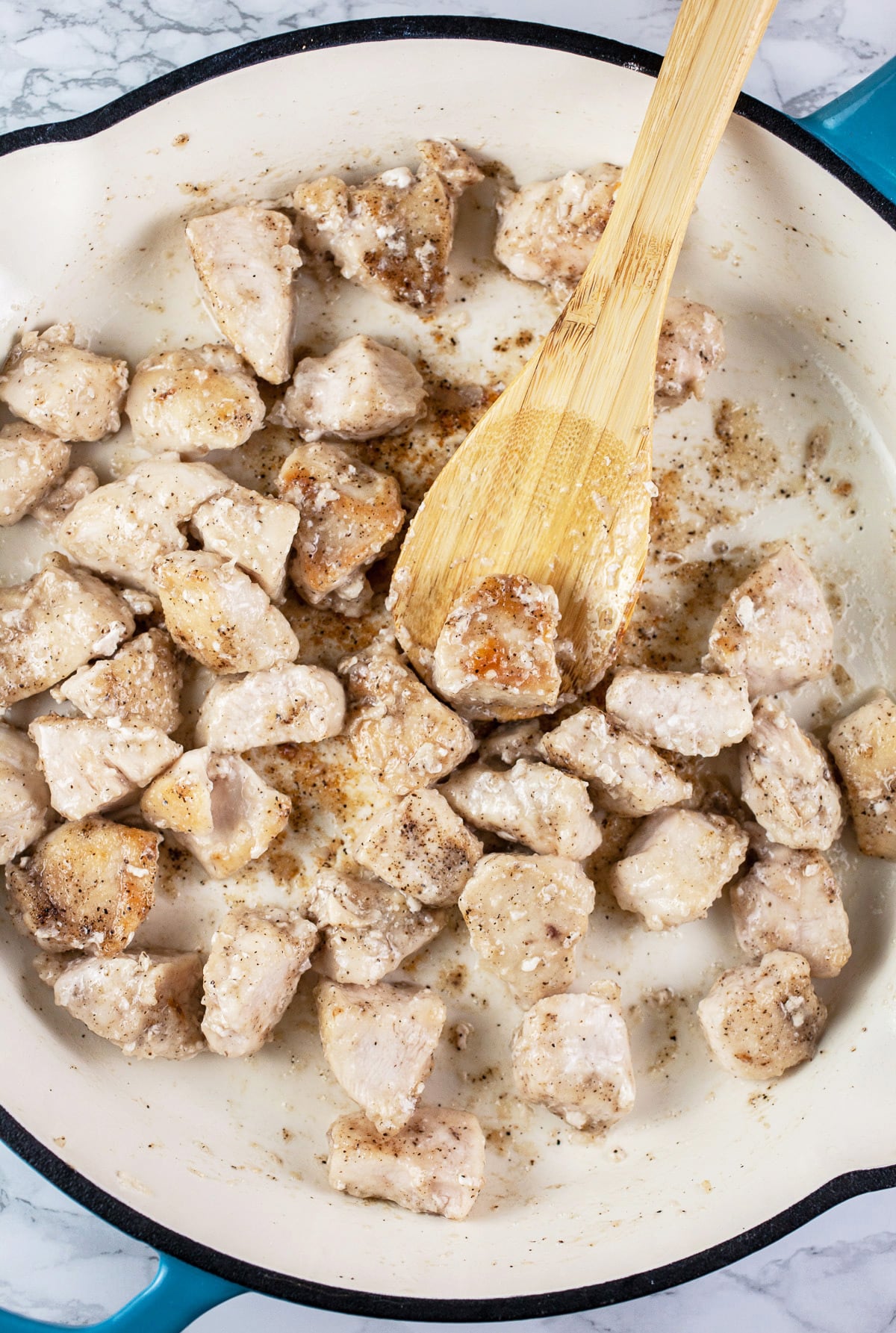 Chicken sautéed in skillet with wooden spoon.