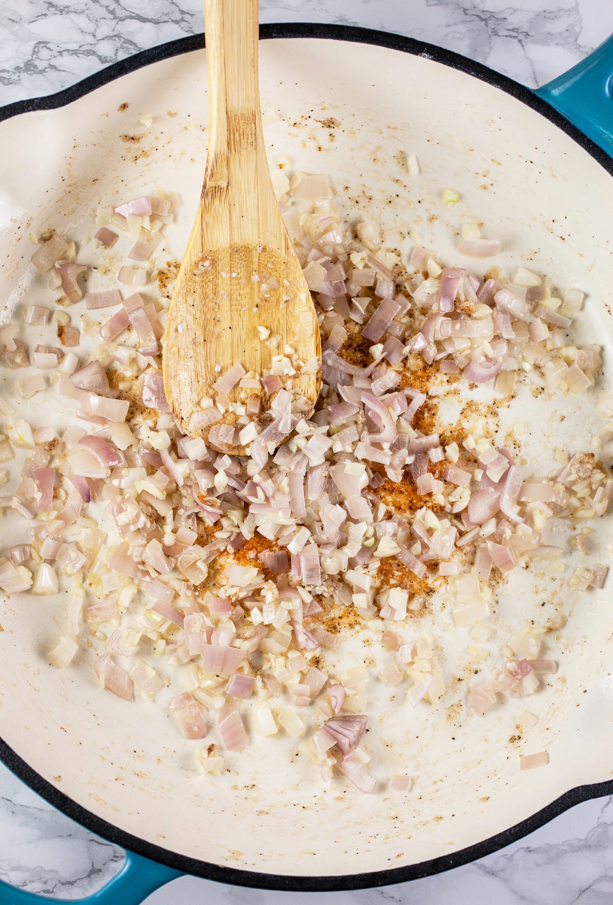 Garlic and shallots sautéed in skillet with wooden spoon.