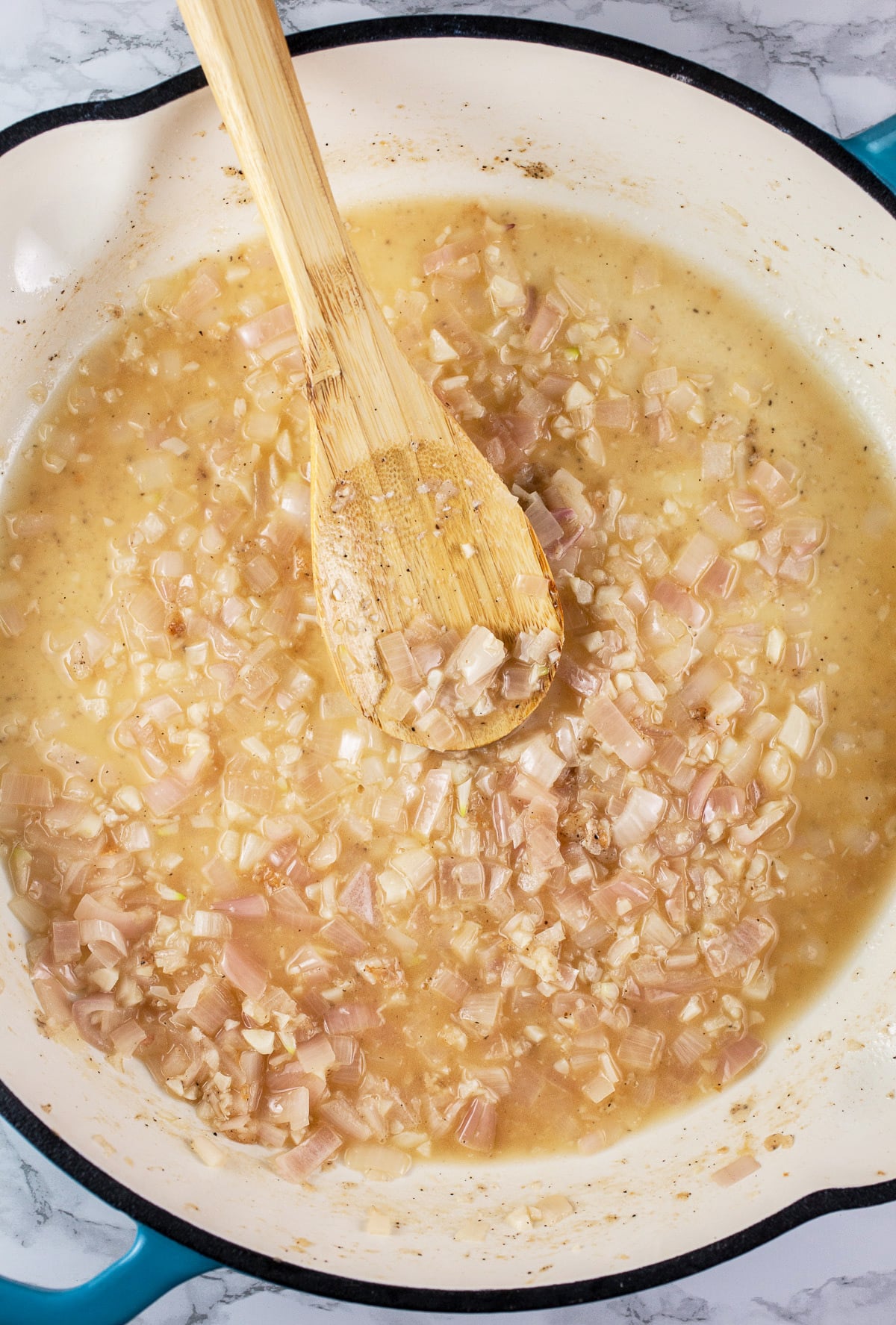 Garlic, shallots, and wine sautéed in skillet with wooden spoon.