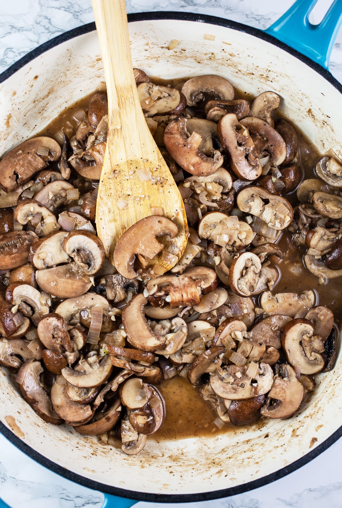 Mushrooms and wine sautéed in skillet with wooden spoon.