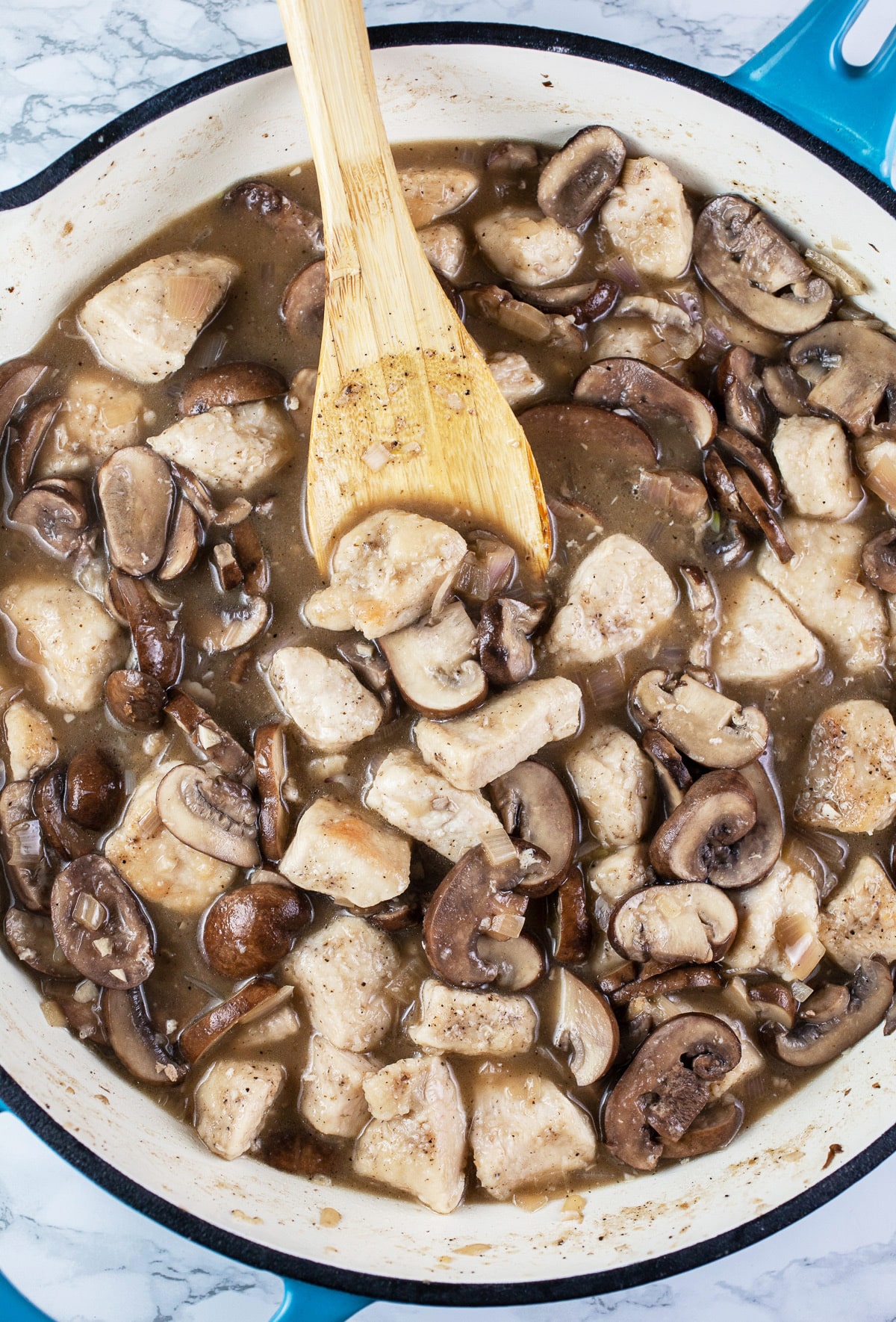 Chicken and mushrooms simmered in skillet with wooden spoon.