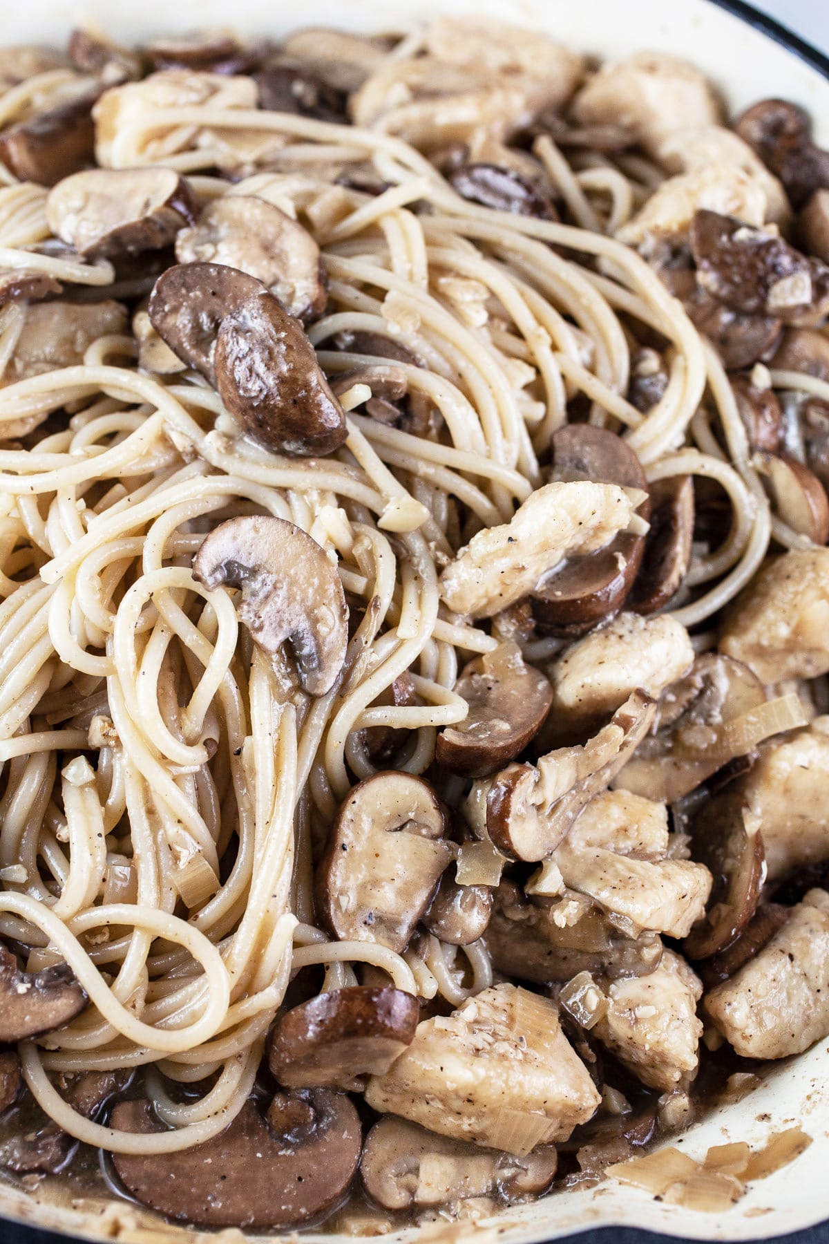 Spaghetti noodles, mushrooms, and chicken tossed together in skillet.