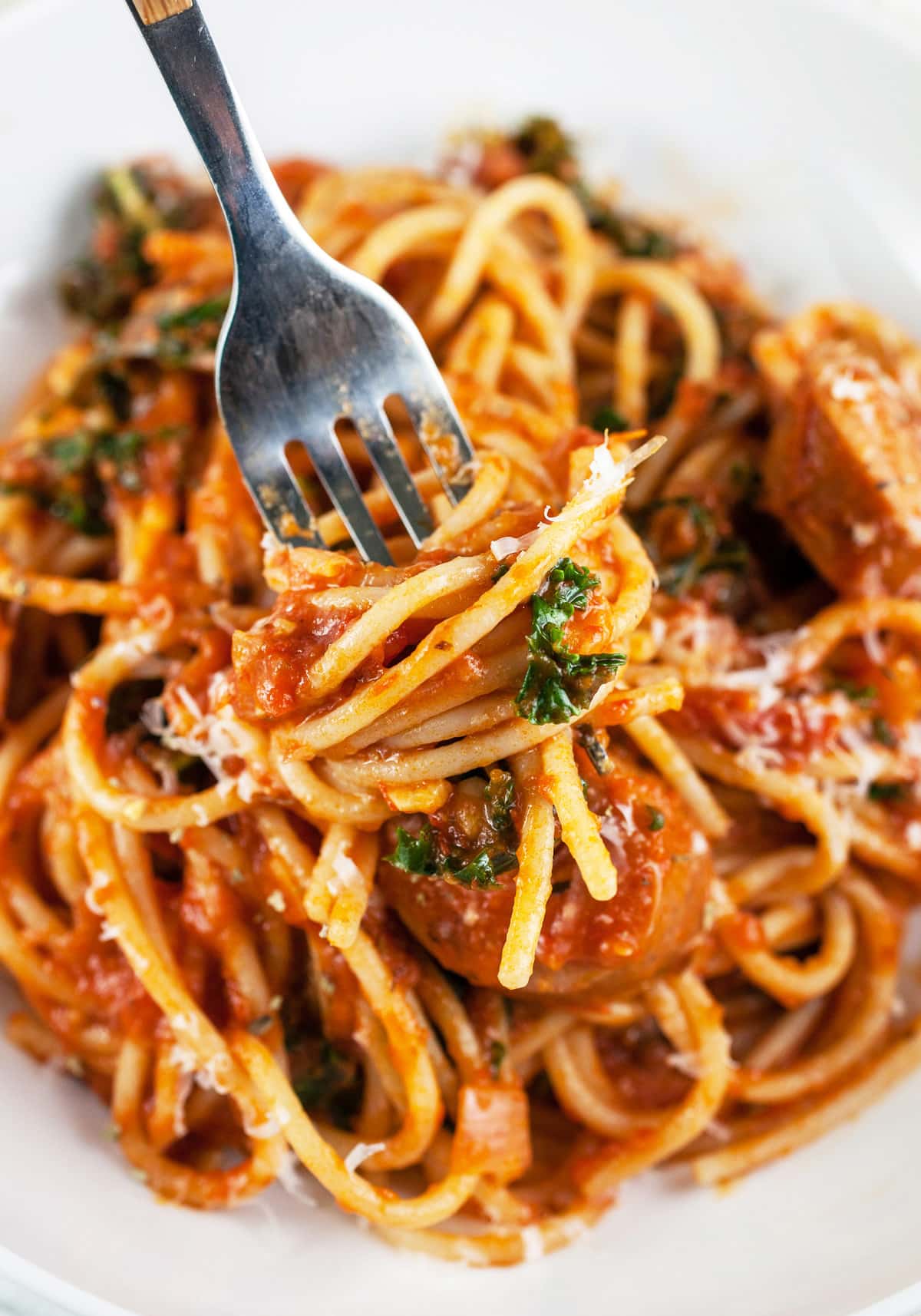 Forkful of sausage spaghetti lifted from white bowl.