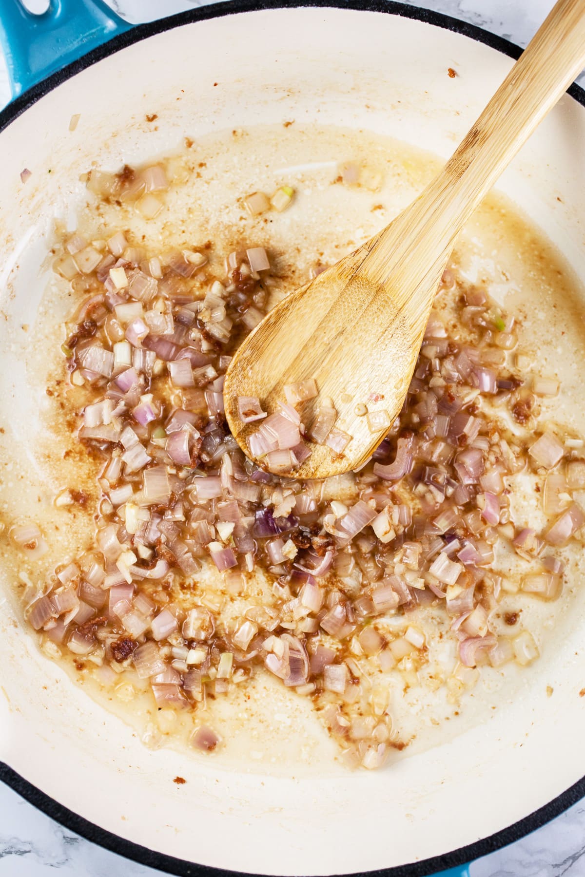 Minced garlic and shallots sautéed in skillet with wooden spoon.