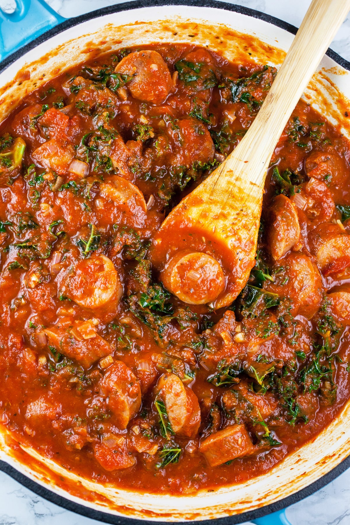 Chicken sausage and kale simmered in spaghetti sauce in skillet.