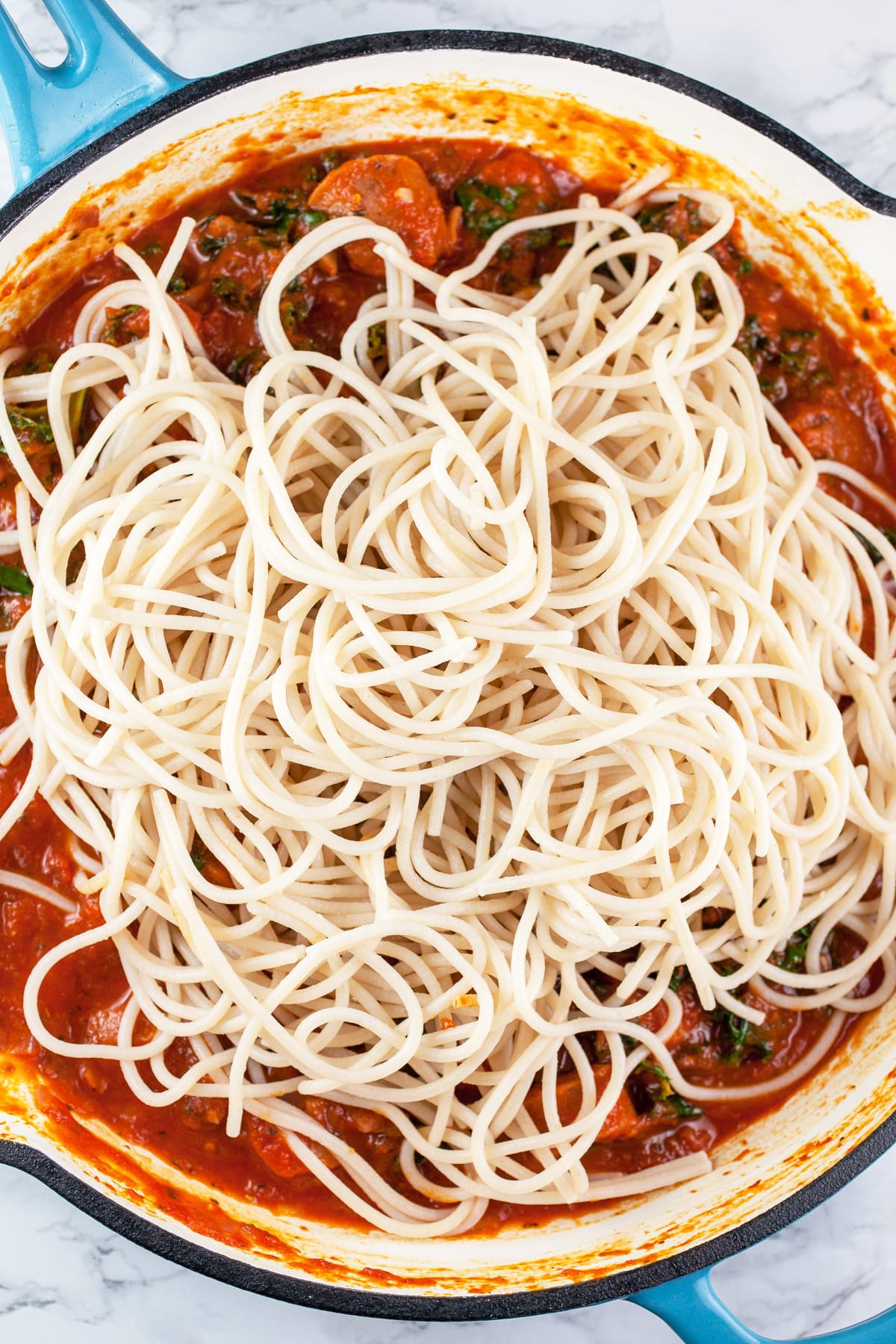 Cooked spaghetti noodles added to sauce in skillet.