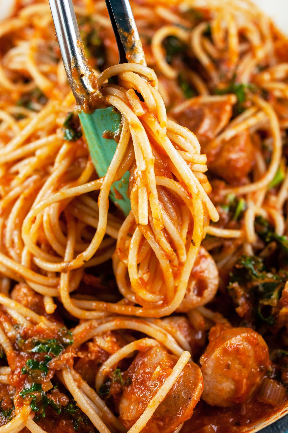 Pasta coated in spaghetti sauce lifted from skillet with tongs.