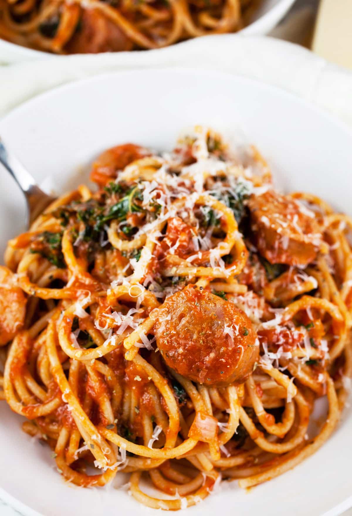 Chicken sausage spaghetti with Parmesan cheese in white bowl.