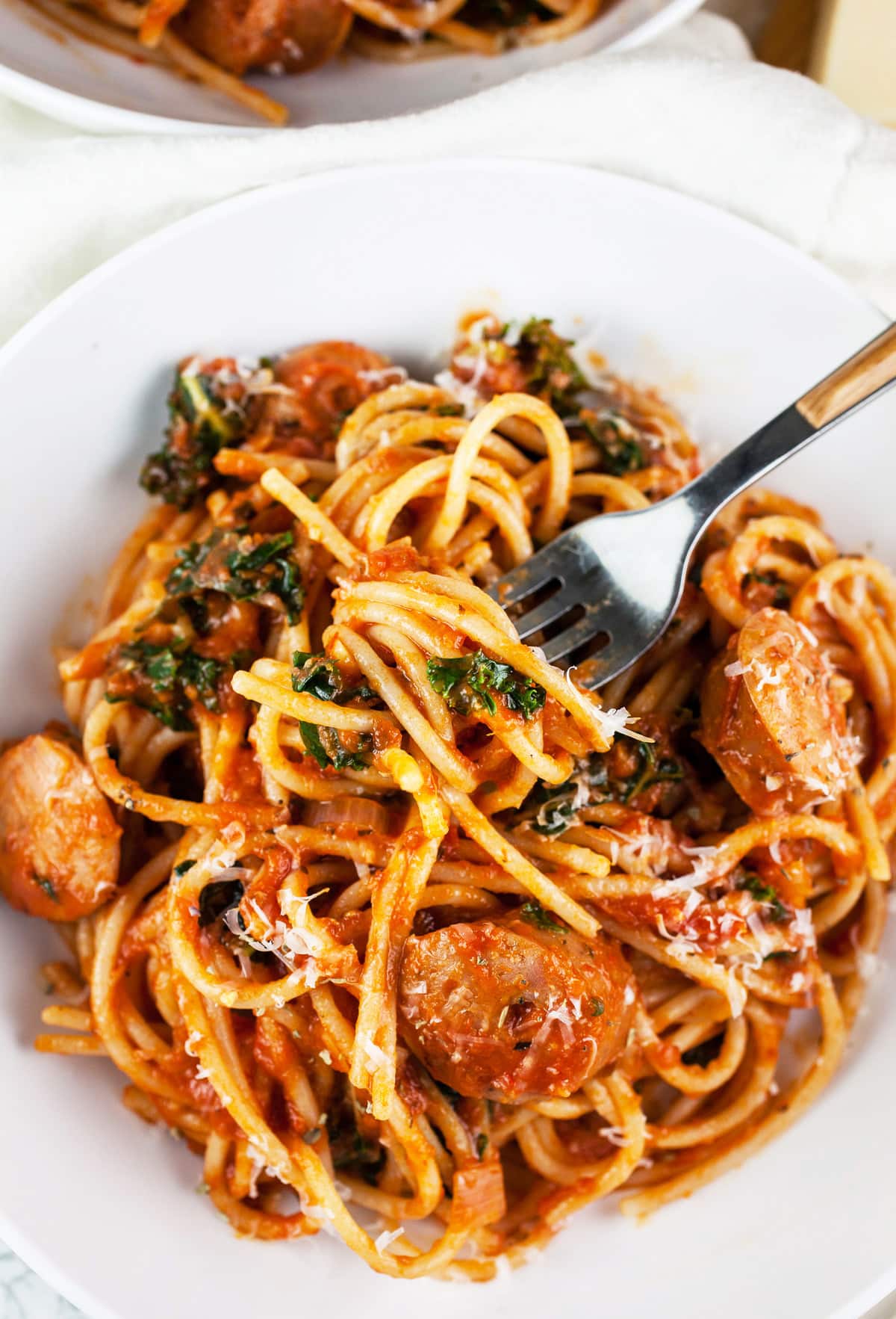 Chicken sausage spaghetti with fork in white bowl.