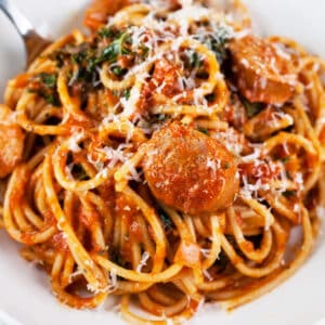 Chicken sausage spaghetti with Parmesan cheese in white bowl.