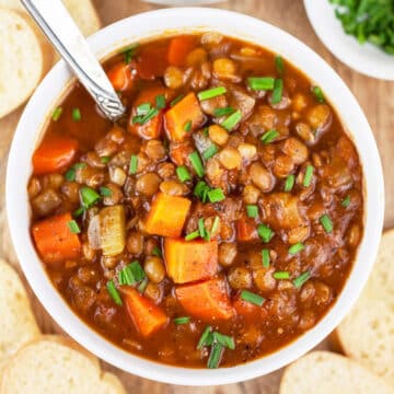 Hearty lentil soup in white bowl with spoon.