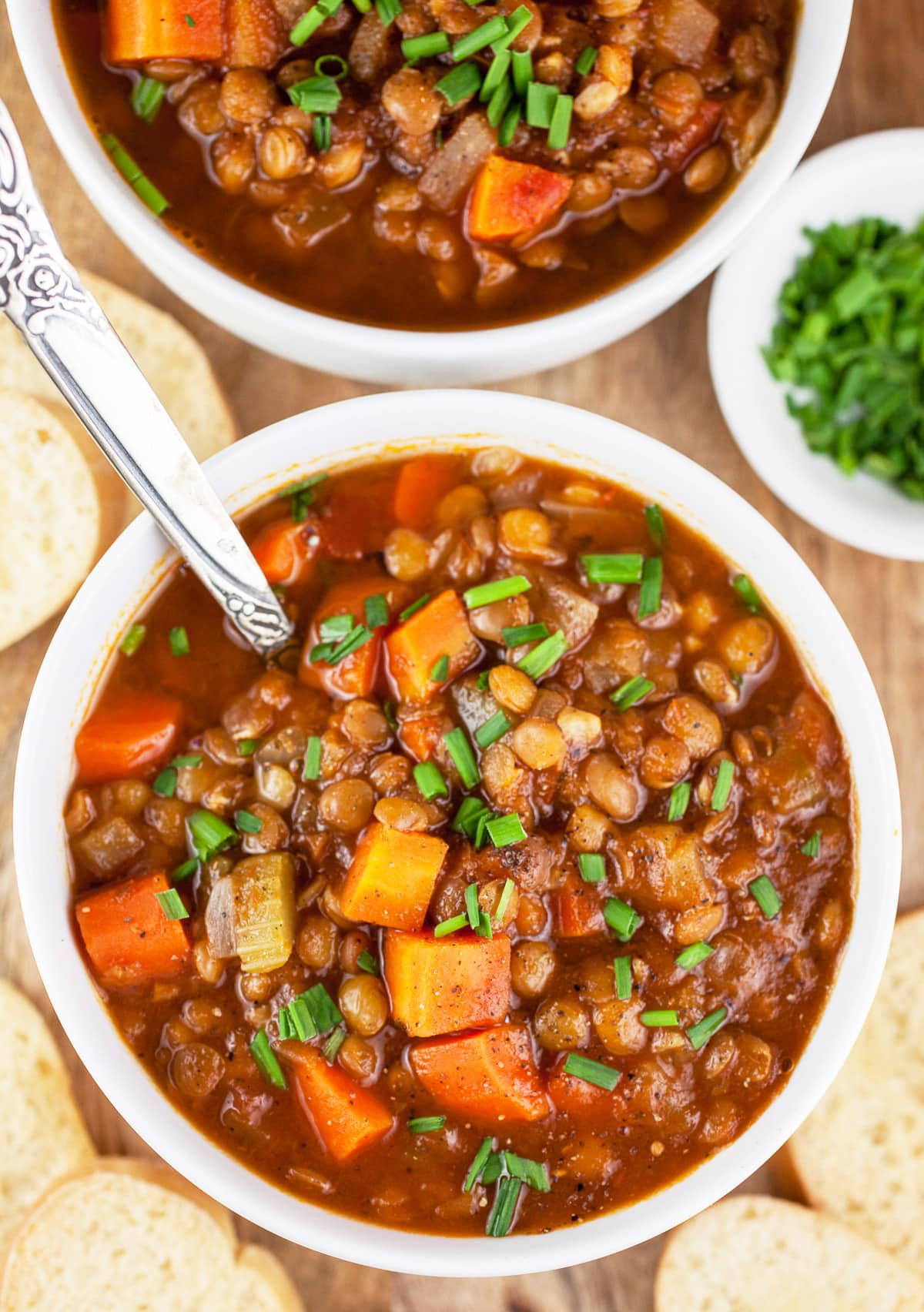 Hearty lentil soup in white bowls with minced chives and sliced bread.