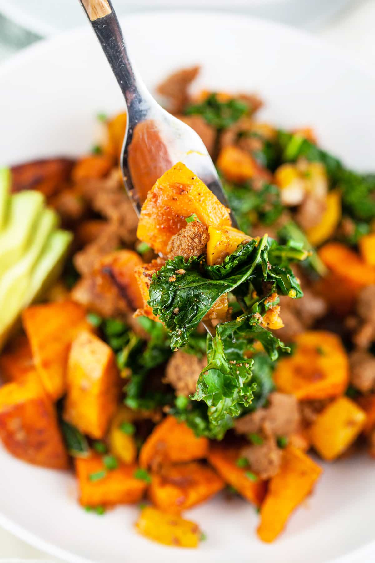 Forkful of sweet potato kale hash lifted from white bowl.