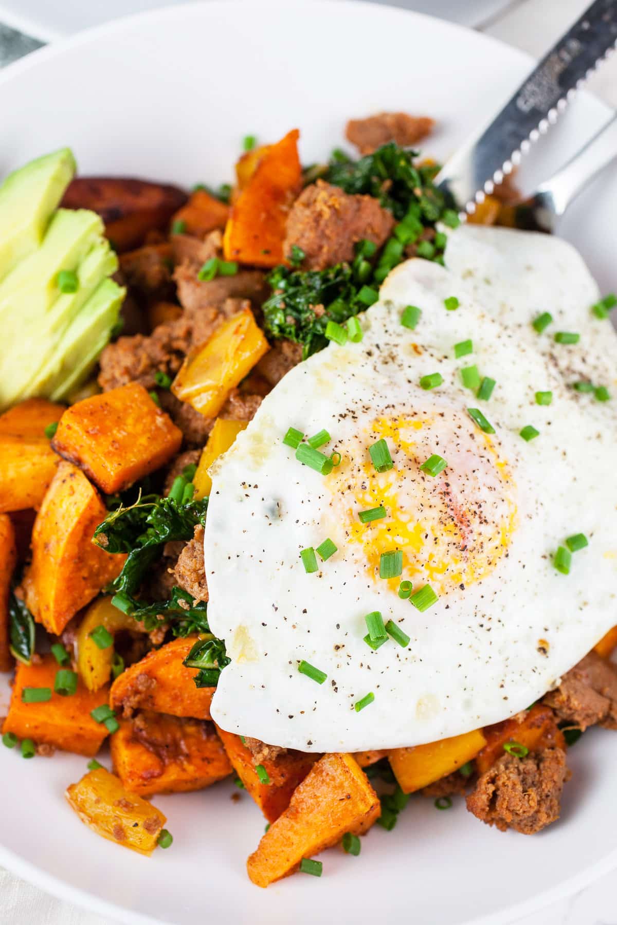 Over easy egg on top of sweet potato hash in white bowl with fork.