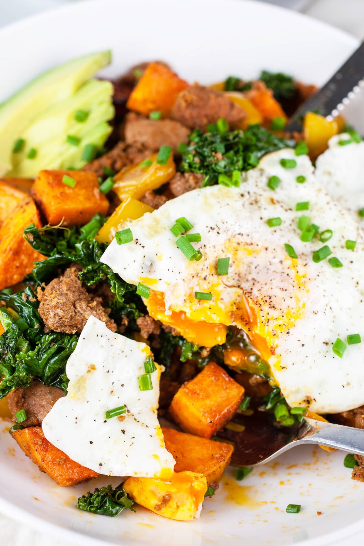 Sweet potato turkey hash with over easy egg cut in half with fork.