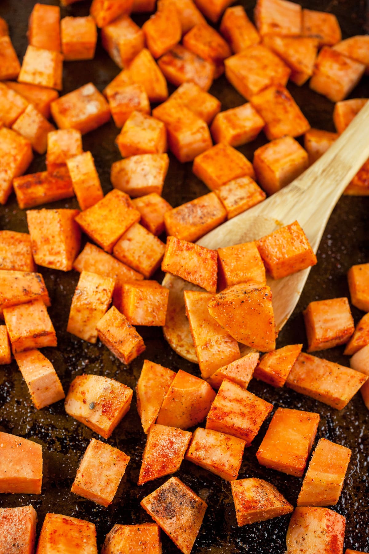Uncooked diced sweet potatoes on baking sheet with wooden spoon.