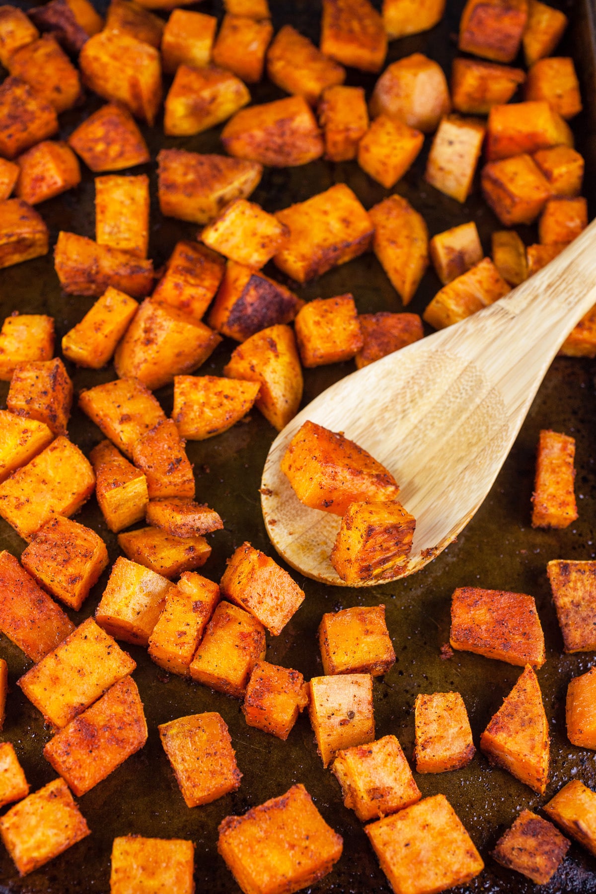 Roasted diced sweet potatoes on baking sheet with wooden spoon.