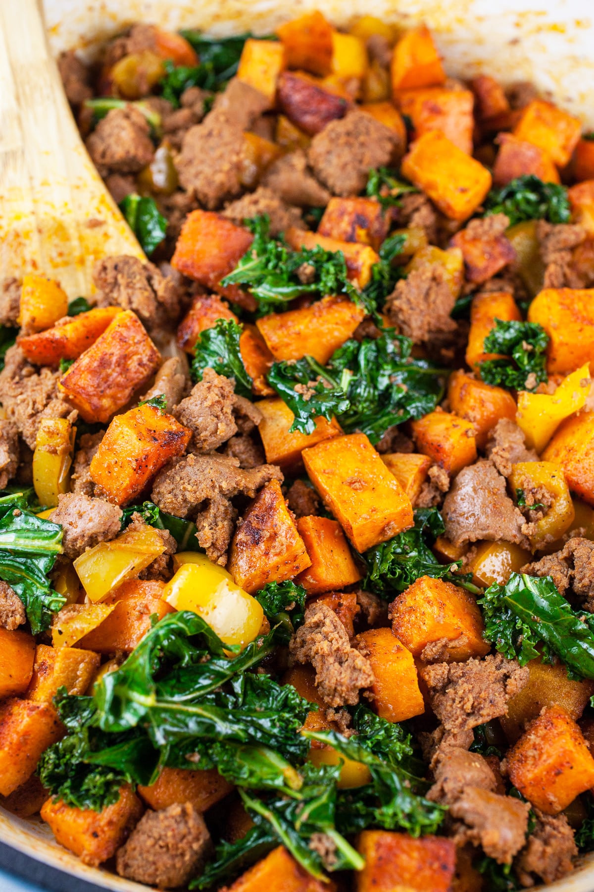 Sweet potato turkey hash in skillet with wooden spoon.