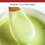 Cashew cilantro sauce lifted with wooden spoon from white bowl.