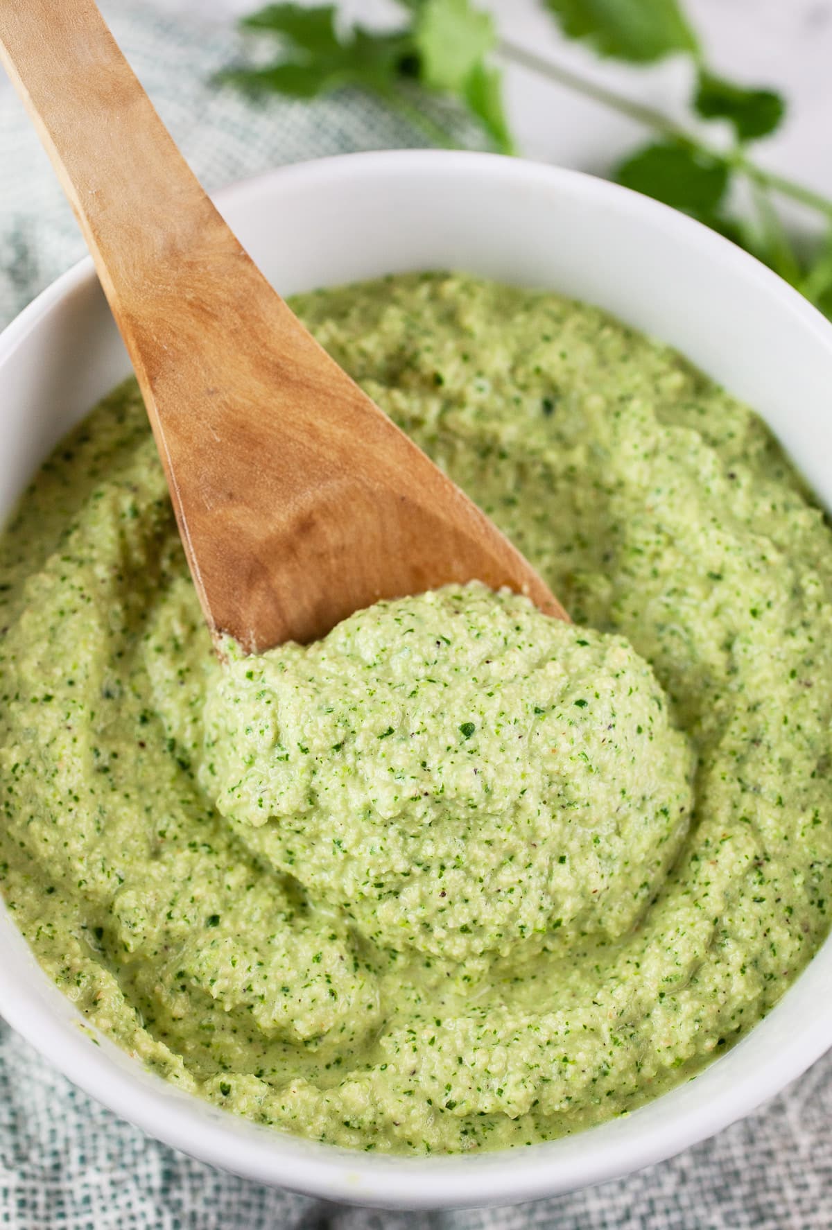 Cashew cilantro sauce with wooden spoon in white bowl.