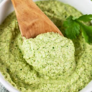 Cashew cilantro sauce with wooden spoon in small white bowl.