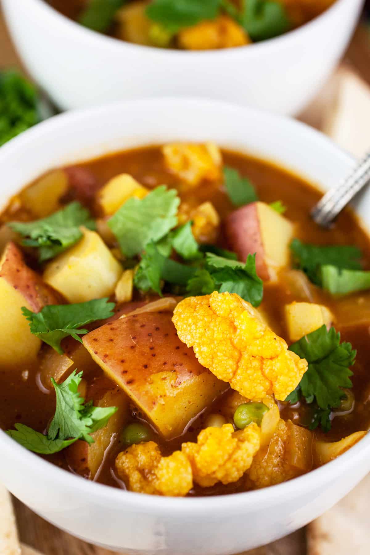 Curried cauliflower potato soup with cilantro in white bowls.