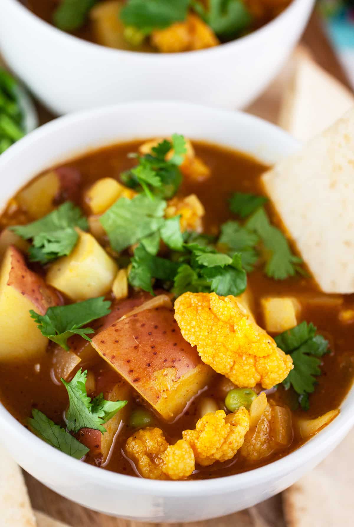 Curried potato cauliflower soup with slice of pita bread in white bowl.